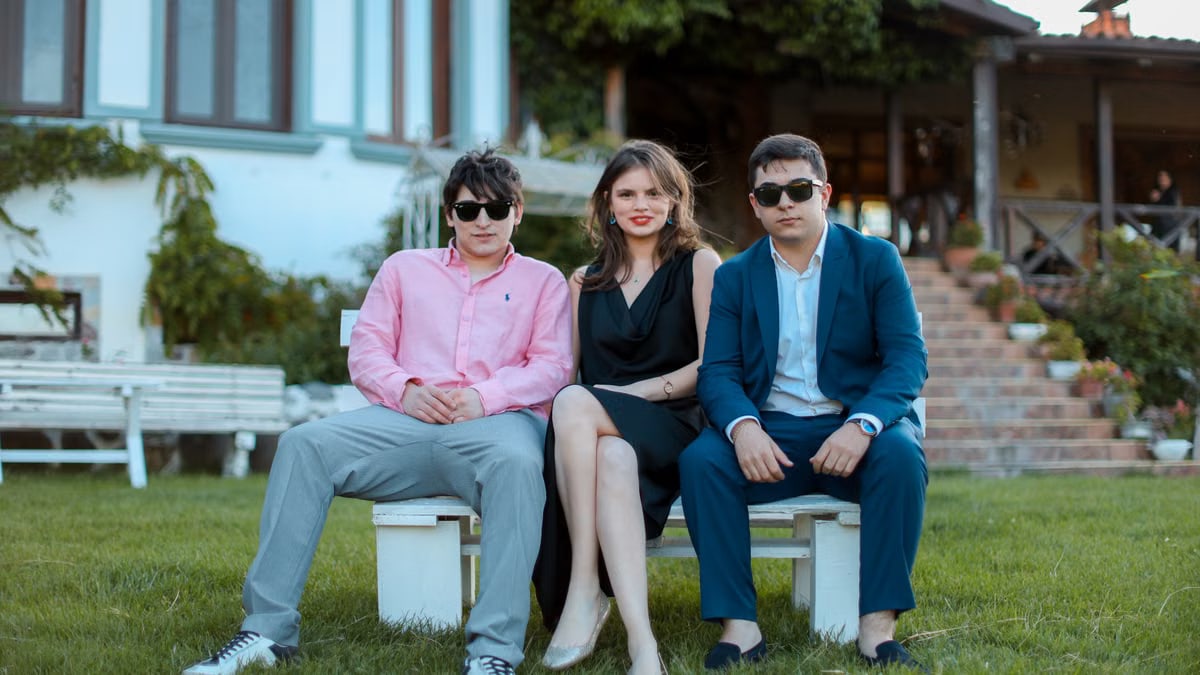 Three young adults in formal attire sitting on benches outdoors, showcasing elegance and friendship.